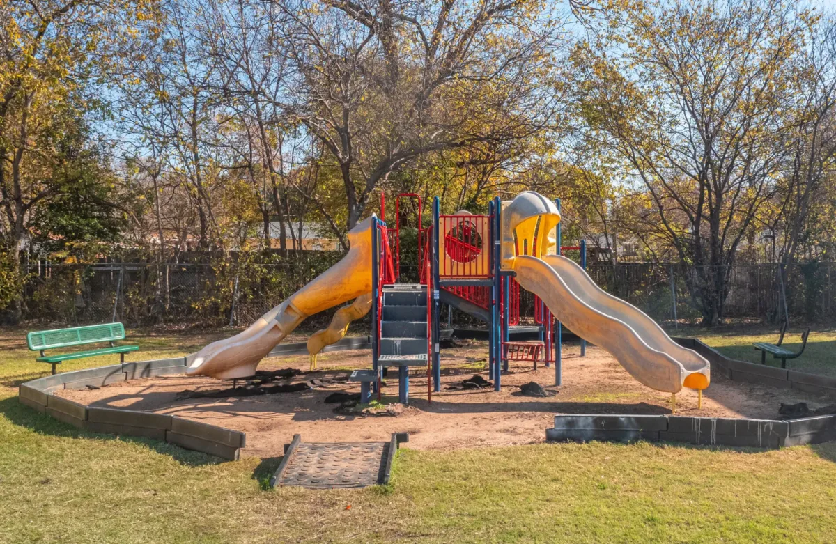 Children's playground with dual slides and benches under mature trees
