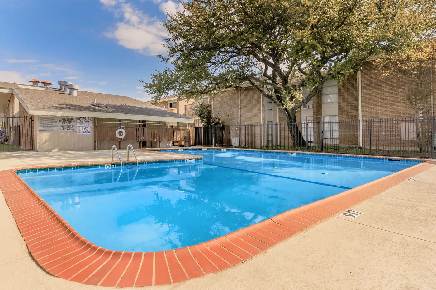 Corner of the swimming pool with brick coping and shade trees overhead