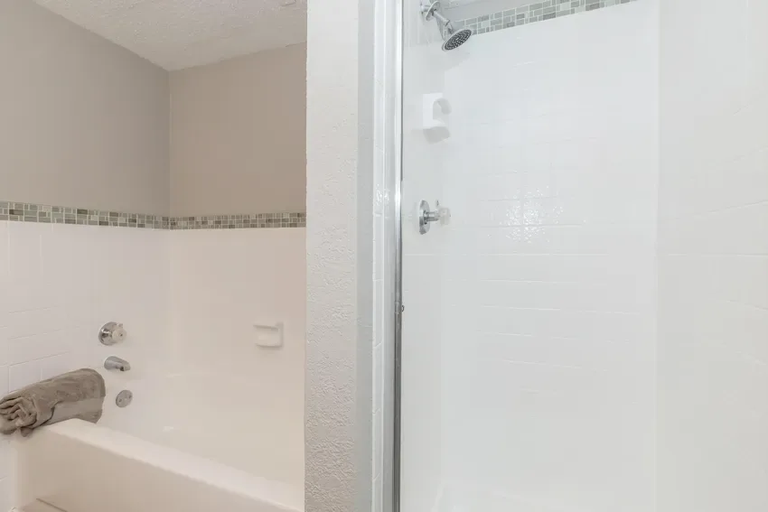Glass-enclosed shower beside a soaking tub with a mosaic-tile accent stripe