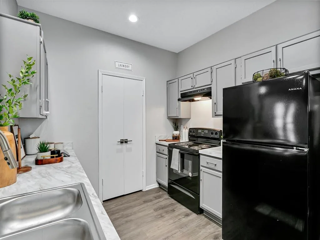 Galley kitchen with light gray cabinets, black range and refrigerator, and wood-style flooring