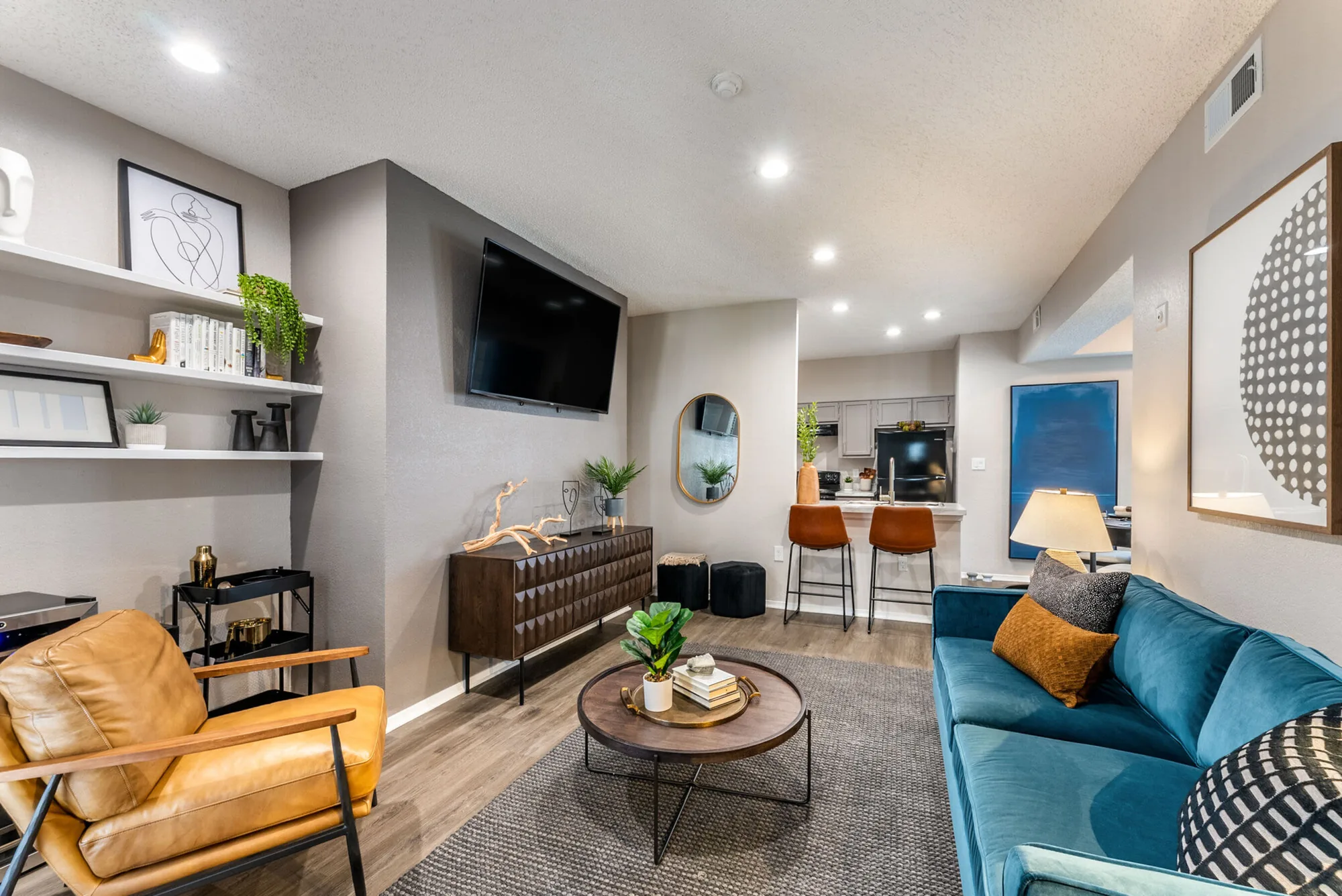 Open living room with a teal velvet sofa, leather armchair and a breakfast bar beyond